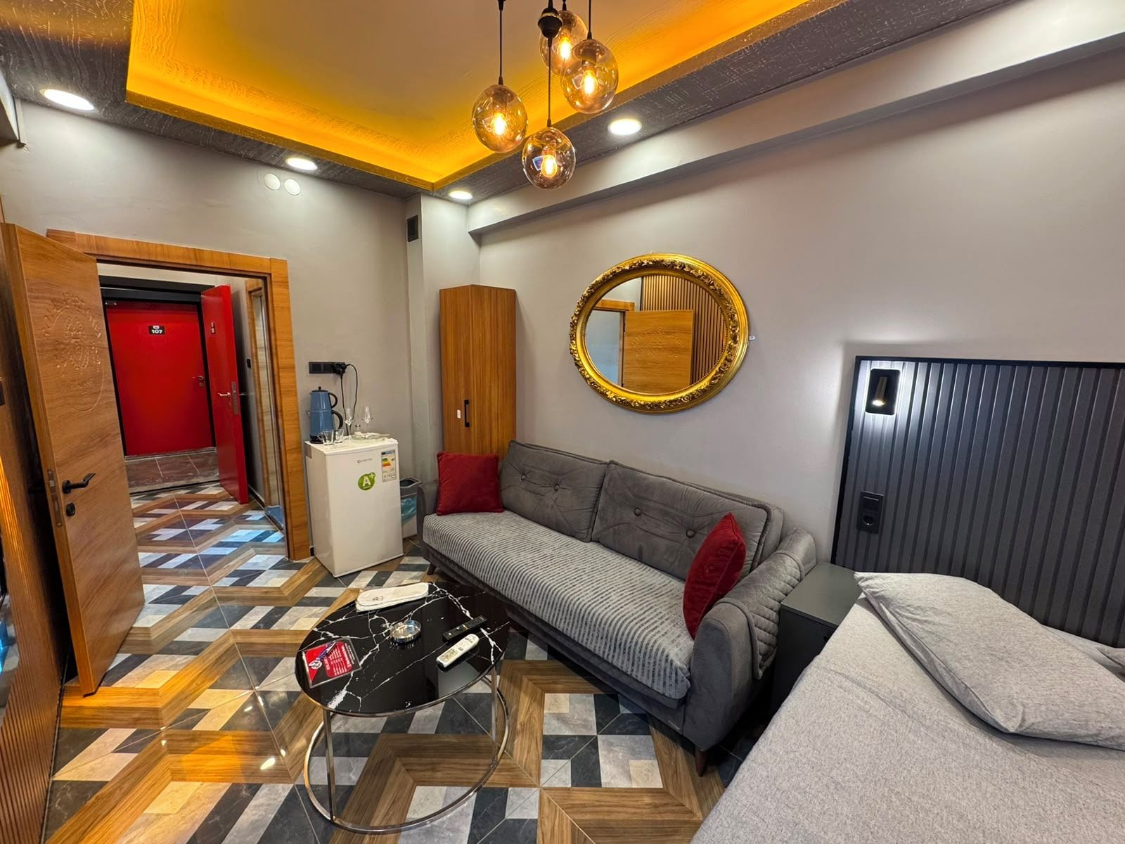 A hotel room with a sofa, a bed, a coffee machine, a mirror, and a patterned floor.