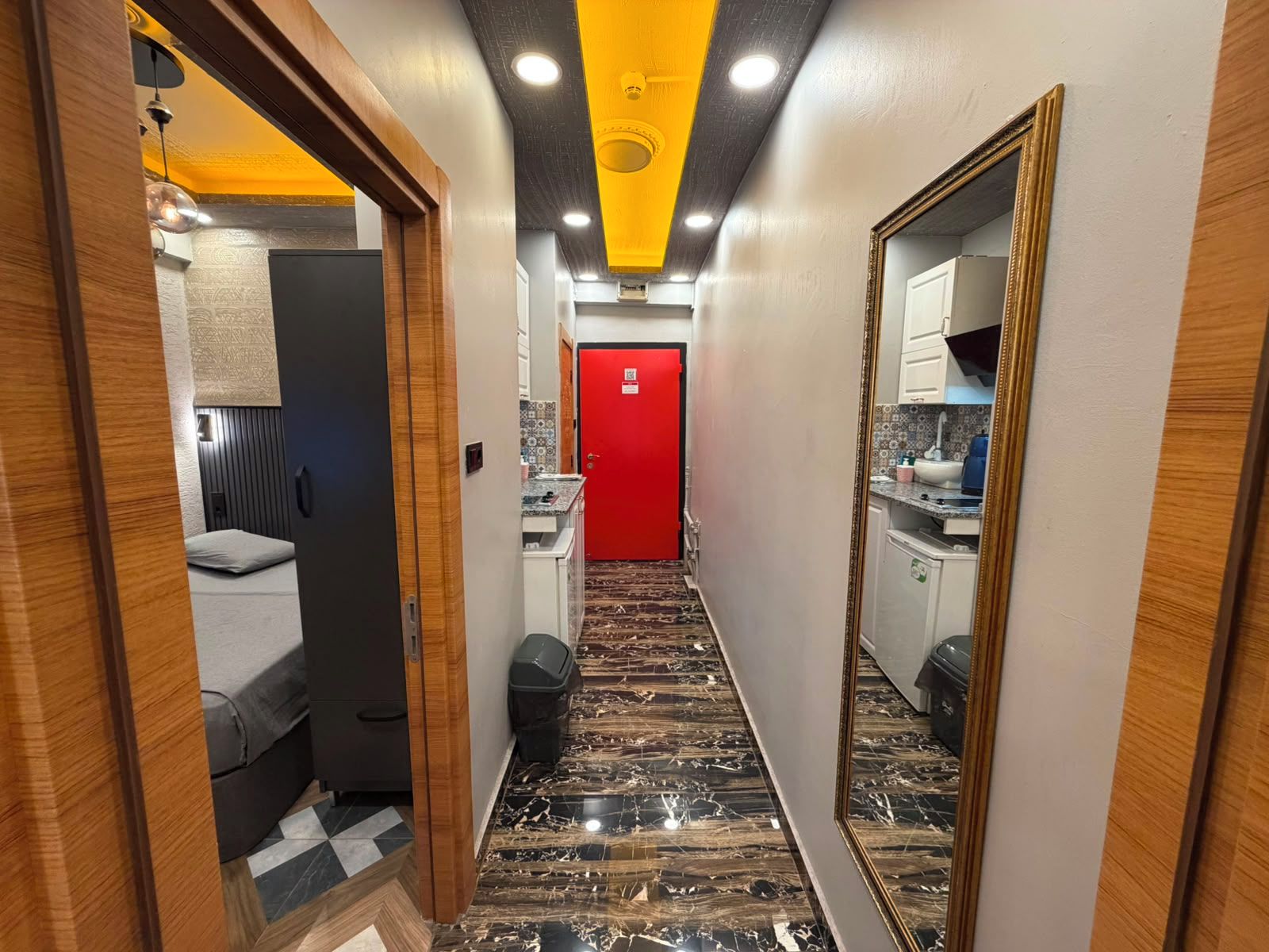 A hallway with a red door, a mirror, and a patterned floor.