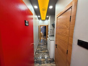 Ein Hotelkorridor mit roter Wand, einer Nummer, einer Holztür mit geprägter Beschriftung und einem Marmorboden.
