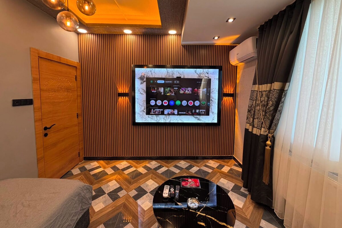 A modern room with a flat-screen TV mounted on the wall, a wooden door, a patterned floor, and a small table with a remote control.