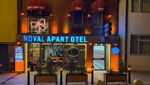 A Royal Apart Hotel with a prominent neon sign, a reception area, and a balcony with red umbrellas.