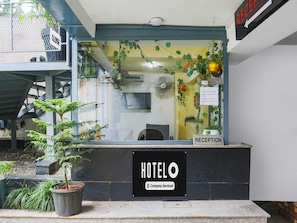 Ein Hotel-Rezeptionsbereich mit einer Rezeption, einem Schild mit der Auscheckzeit und einem Schild für das Hotel 'HOTEL O'.