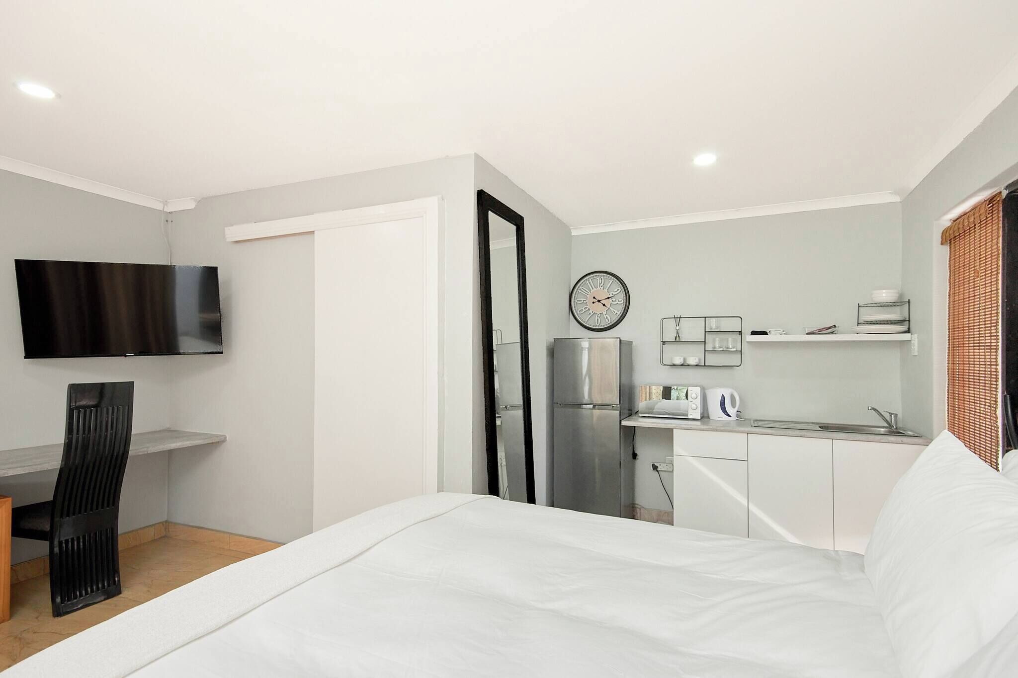 A hotel room with a bed, a desk, a television, a refrigerator, a microwave, and a small kitchenette.