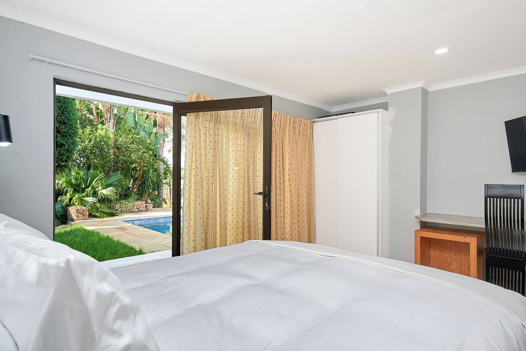 A bedroom with a large bed, a sliding door to a balcony, and a TV mounted on the wall.