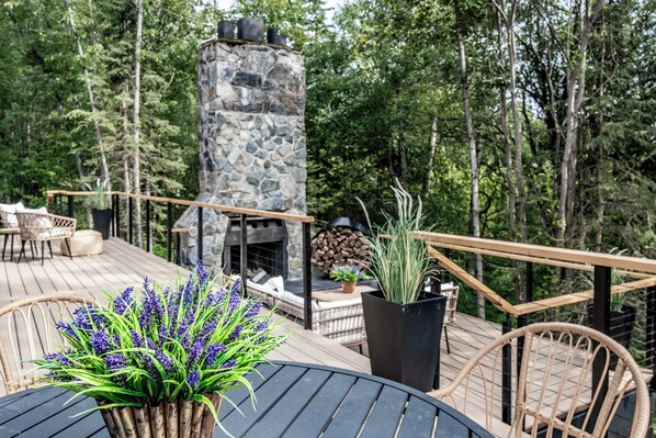 Una terraza con mobiliario exterior, una chimenea de piedra y vistas del bosque circundante.
