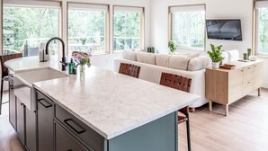Eine moderne Küche mit Marmorarbeitsplatte, integriertem Spülbecken und einem Essbereich mit hellem Sofa und einem Holzsideboard.