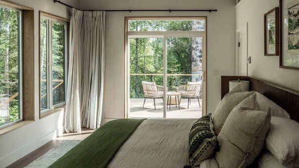 Ein Schlafzimmer mit einem großen Bett, Blick ins Freie durch eine Schiebetür und einem Balkon mit Sitzgelegenheiten.