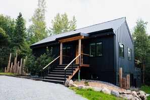 A modern two-story building with a black exterior, wooden staircase, and a gravel driveway. - The Aspens at Meadow Creek (Anchorage)