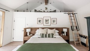 Ein Schlafzimmer mit erhöhter Schlafkoje, einem Bett mit vielen Kissen, Nachttischen mit Lampen und gerahmten Kunstwerken an der Wand.