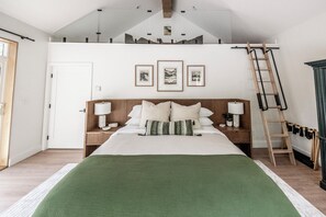 Ein Schlafzimmer mit erhöhter Schlafkoje, einem Bett mit vielen Kissen, Nachttischen mit Lampen und gerahmten Kunstwerken an der Wand.