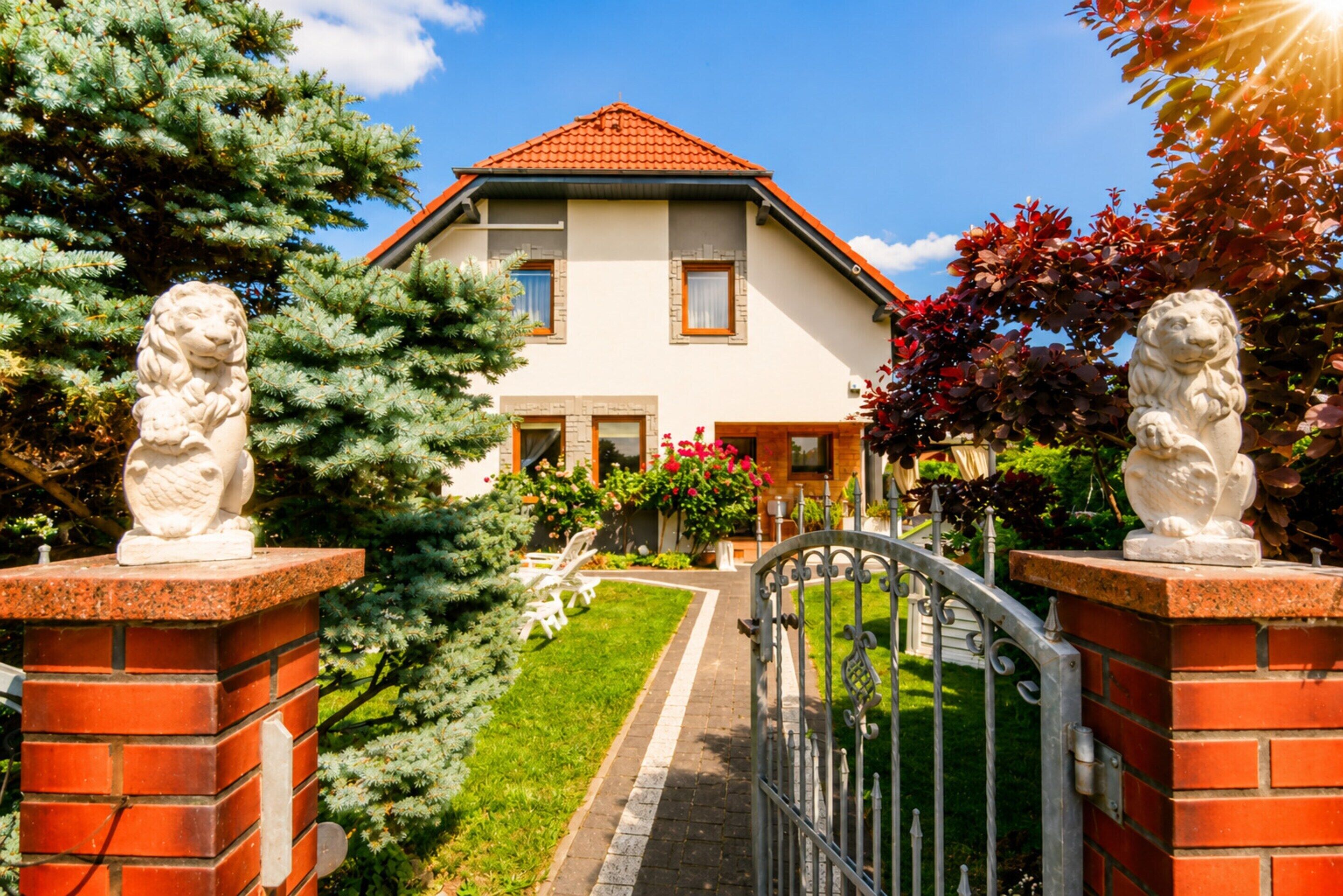 A two-story house with a red-tiled roof, a brick entrance, and a metal gate.