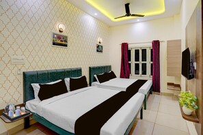 Ein Hotelzimmer mit zwei Betten, einem Deckenventilator, einem Fernseher, einem Fenster mit Vorhängen und einer Wandleuchte.