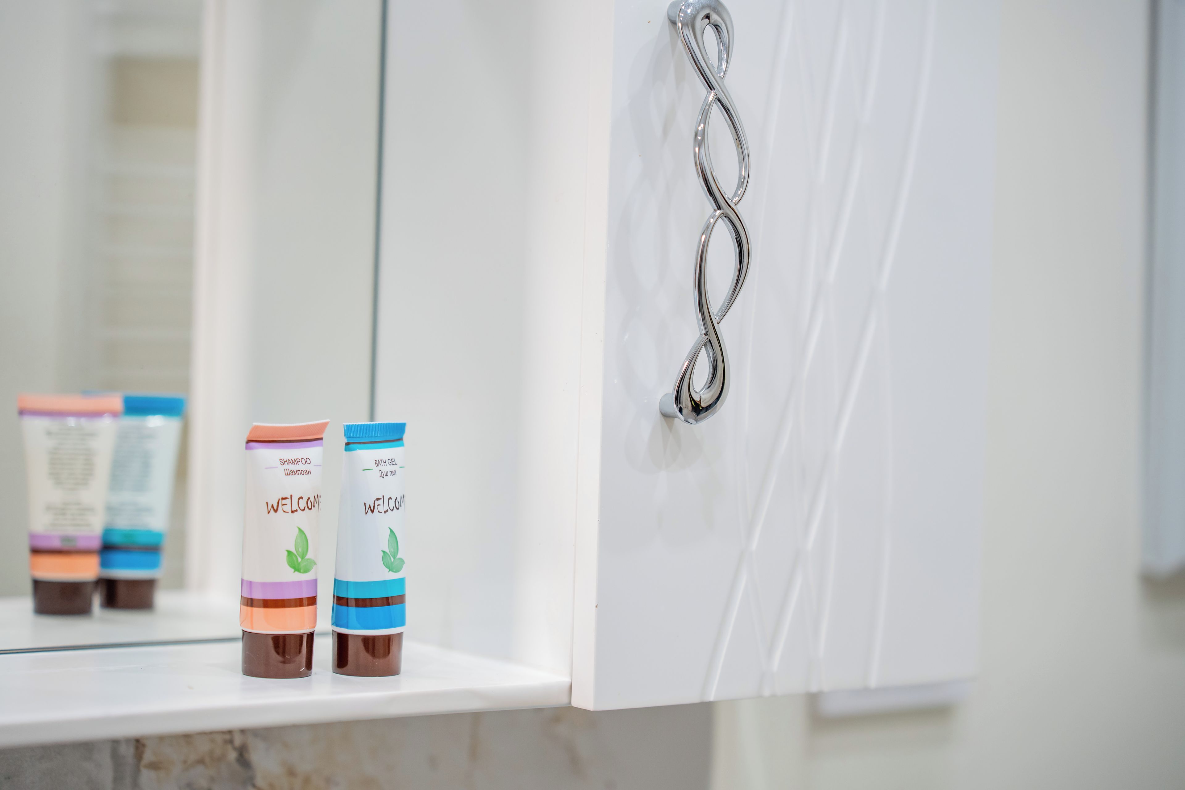 A bathroom with a white vanity, a towel rack, and two bottles of shampoo and bath gel on the counter.