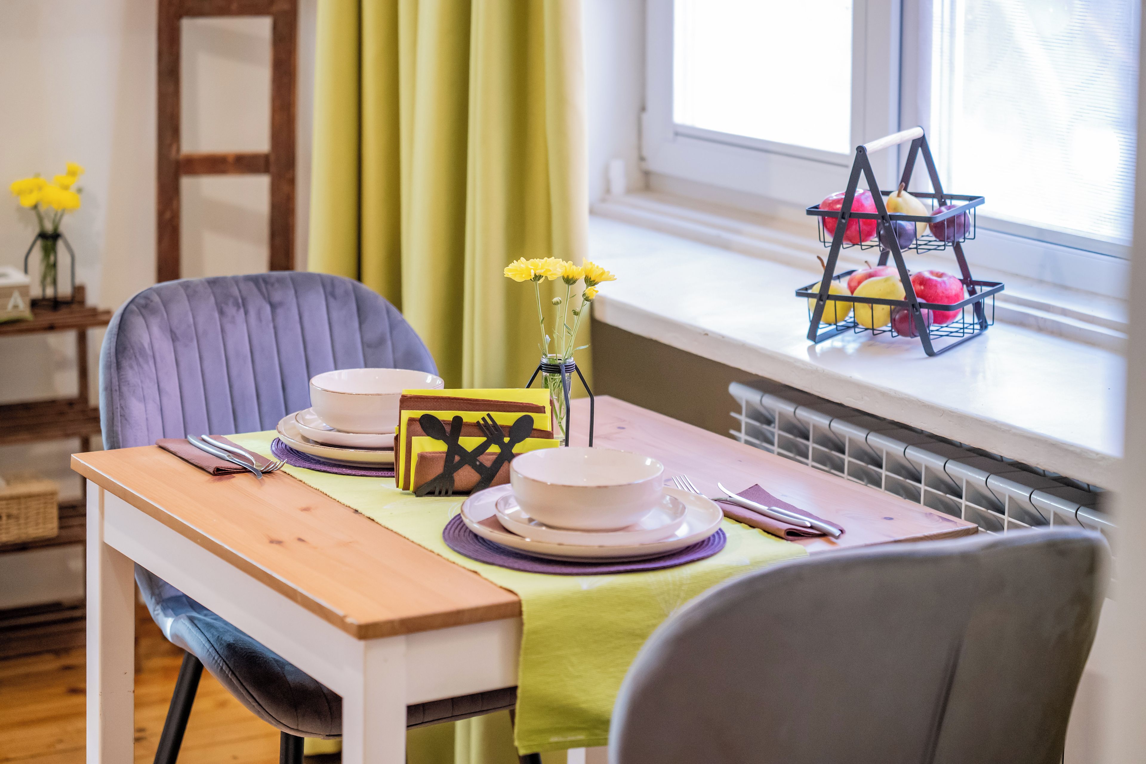A dining table set with plates, bowls, cutlery, and a vase with yellow flowers.