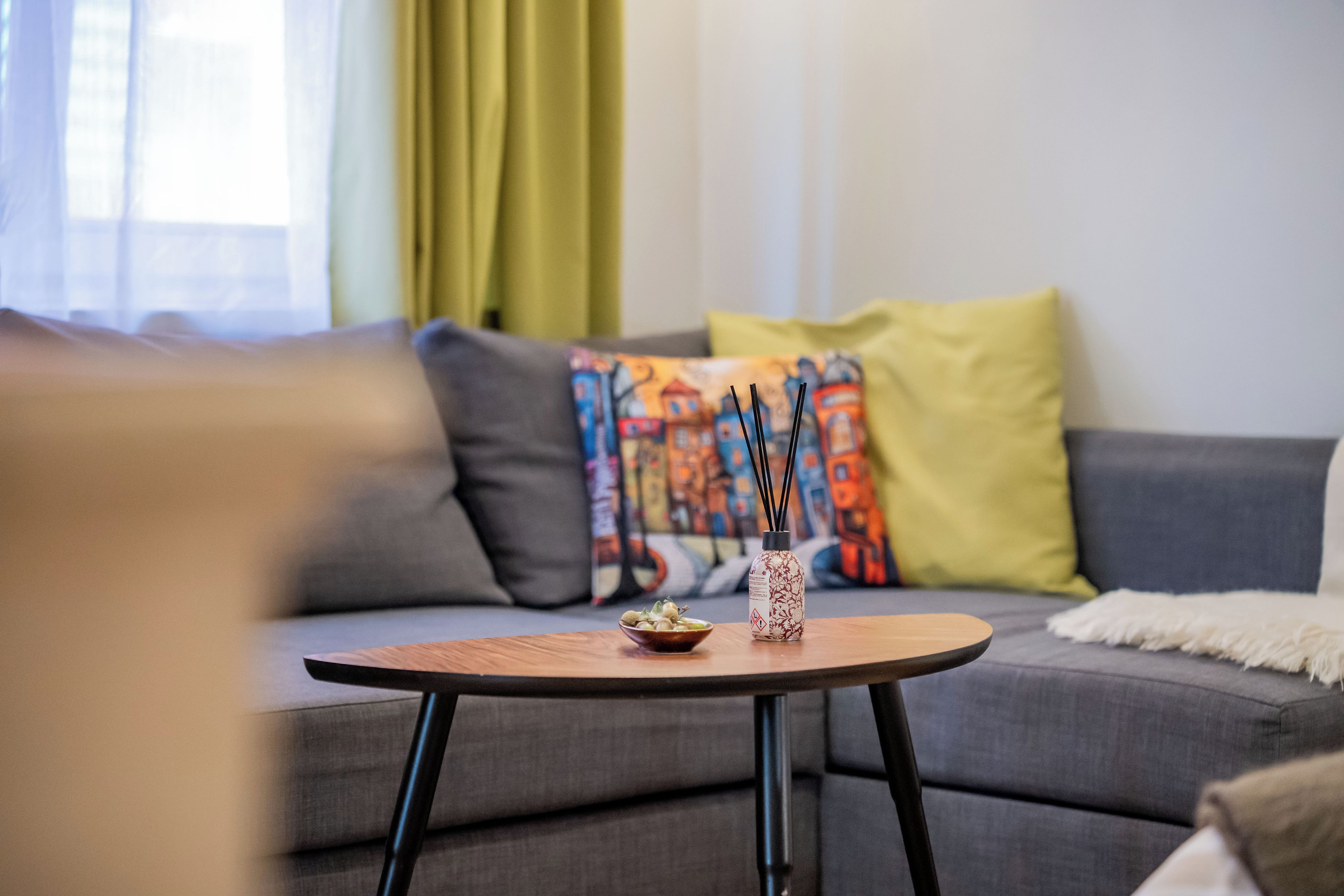 A modern living room with a grey sofa, a round wooden coffee table, and a decorative bottle with reed diffusers.