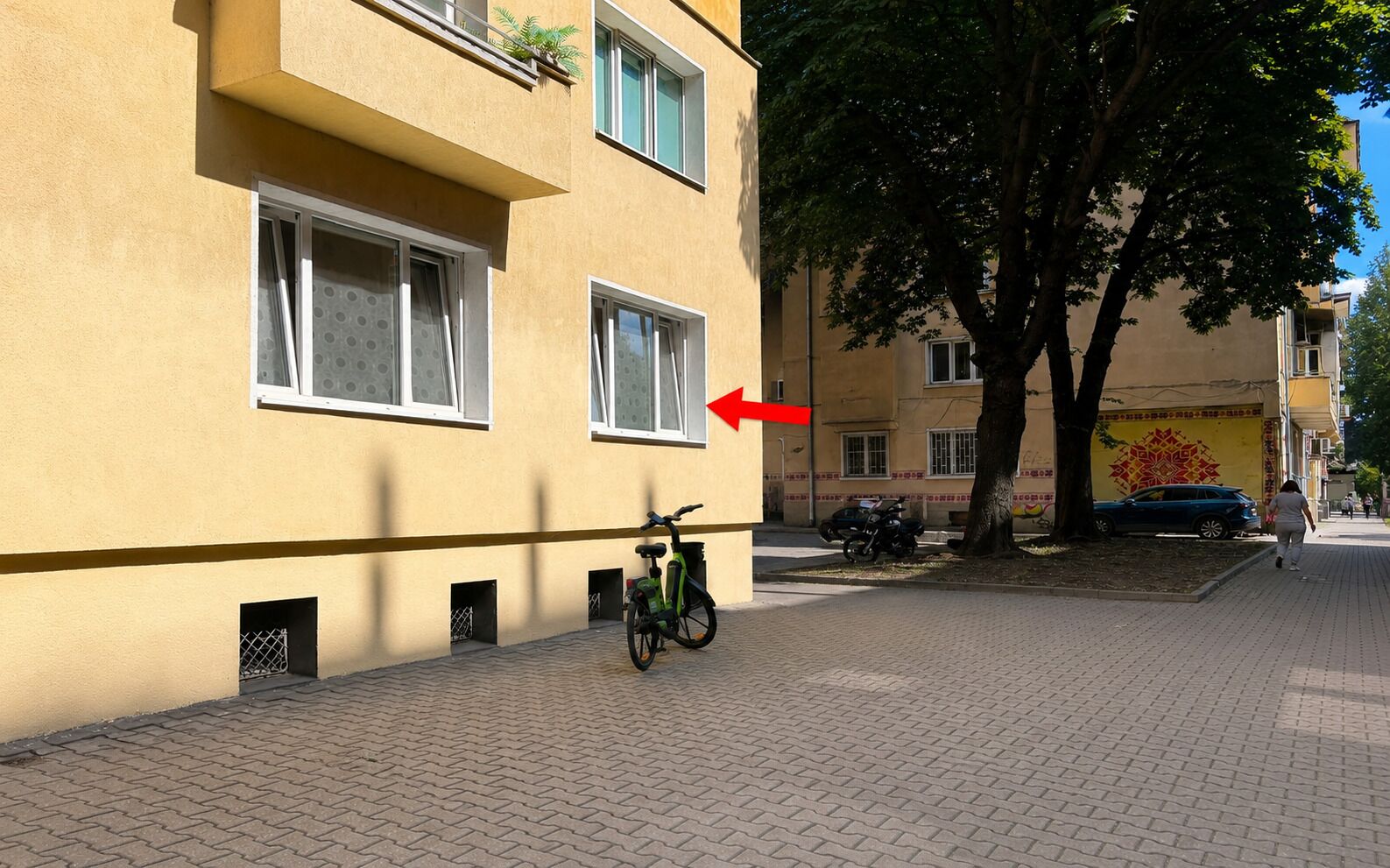 A building with a yellow facade, a bicycle parked in front, and a tree to the right.