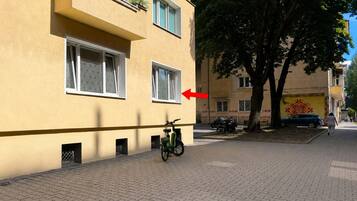 A building with a yellow facade, a bicycle parked in front, and a tree to the right.