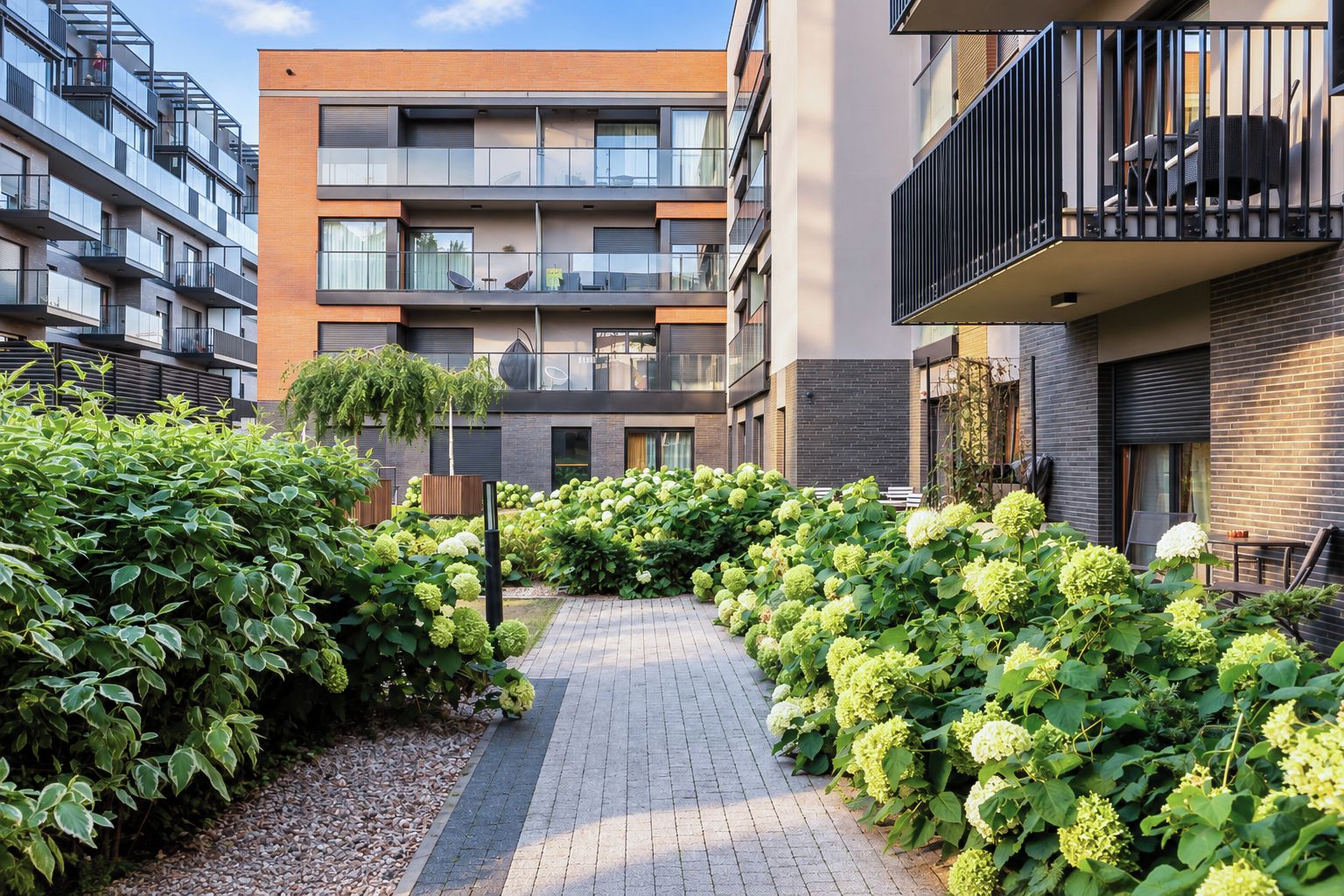 Un immeuble d’appartements moderne doté d’une cour intérieure, d’un espace extérieur aménagé pour s’asseoir et d’une grande variété de plantes.