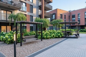 Zona exterior moderna amb una banca de fusta, un enswing i un porxo, tot envoltat de vegetació i un camí pavimentat.
