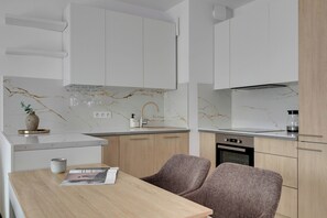 A modern kitchen with white cabinets, a marble backsplash, a built-in oven, and a dining area with a table and chairs. - Riverside Gdańsk Apartment by Lion Apartments (Gdańsk)