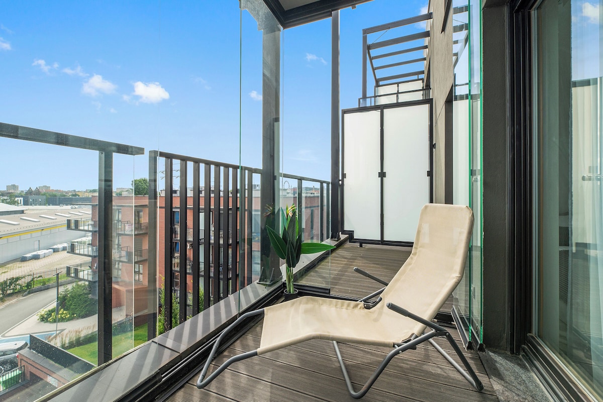 A balcony with a chair, a potted plant, and a view of buildings.