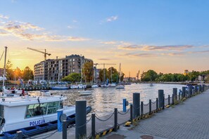 A waterfront marina with boats docked, a police boat, and a building with a crane in the background. - Riverside Gdańsk Apartment by Lion Apartments (Gdańsk)