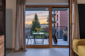 A balcony with a table and chairs, a potted plant, and a view of a building and tree. - Riverside Gdańsk Apartment by Lion Apartments (Gdańsk)