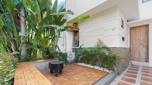 Un cortile con un pontile in legno, un vaso in cemento e diverse piante tropicali.