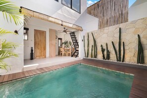Ein moderner Poolbereich im Freien mit einer Holzterrasse, einer Steinwand mit Kakteen und einer Treppe, die zu einer erhöhten Ebene führt.