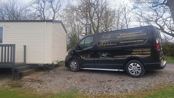 A black van parked in front of a white mobile home with a gravel driveway.