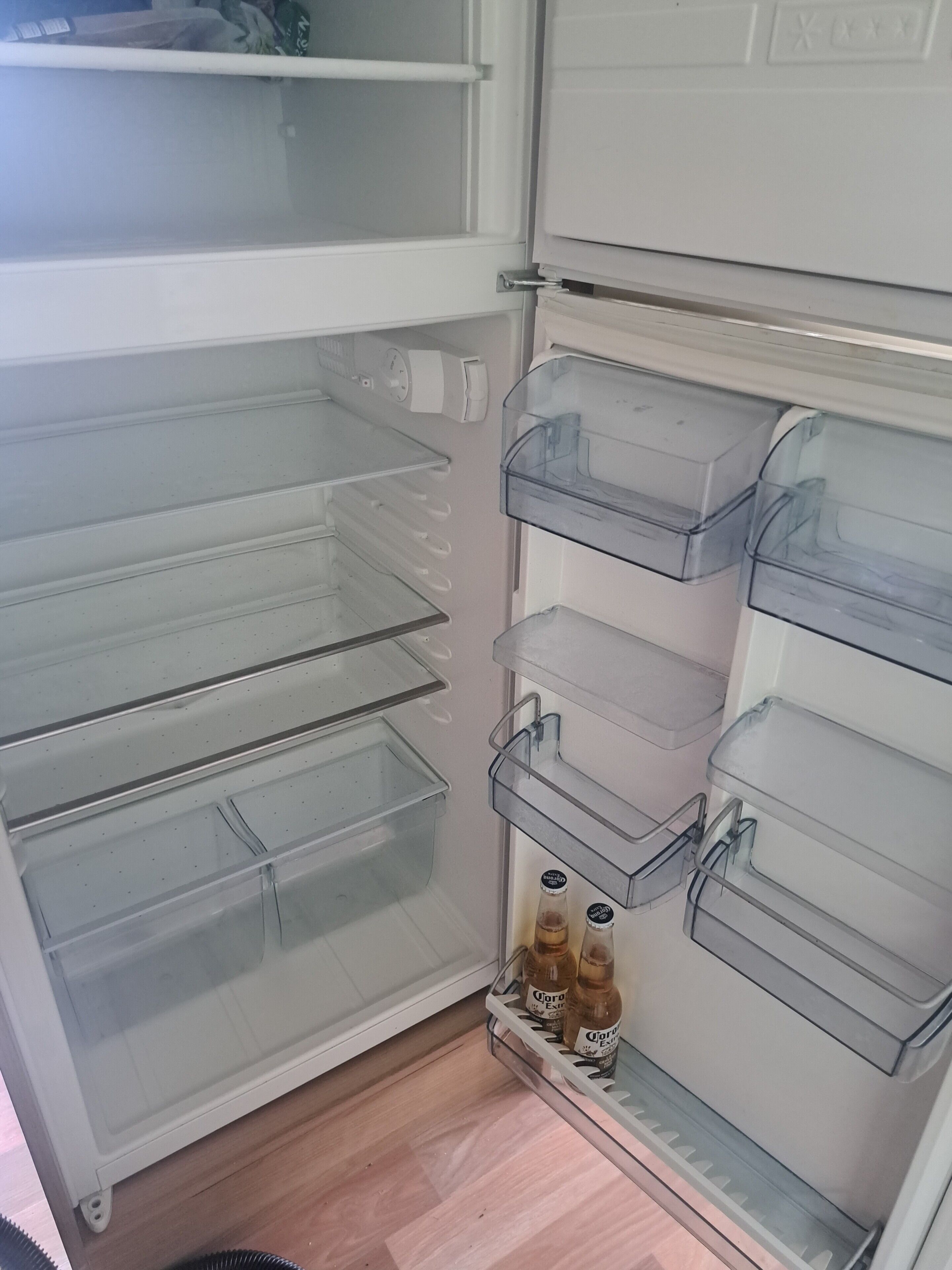 Un réfrigérateur doté de plusieurs tiroirs de rangement transparents et une bouteille de bière Corona sur l’étagère inférieure.