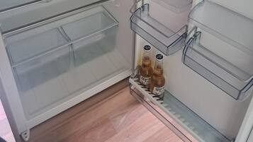 Un réfrigérateur doté de plusieurs tiroirs de rangement transparents et une bouteille de bière Corona sur l’étagère inférieure.