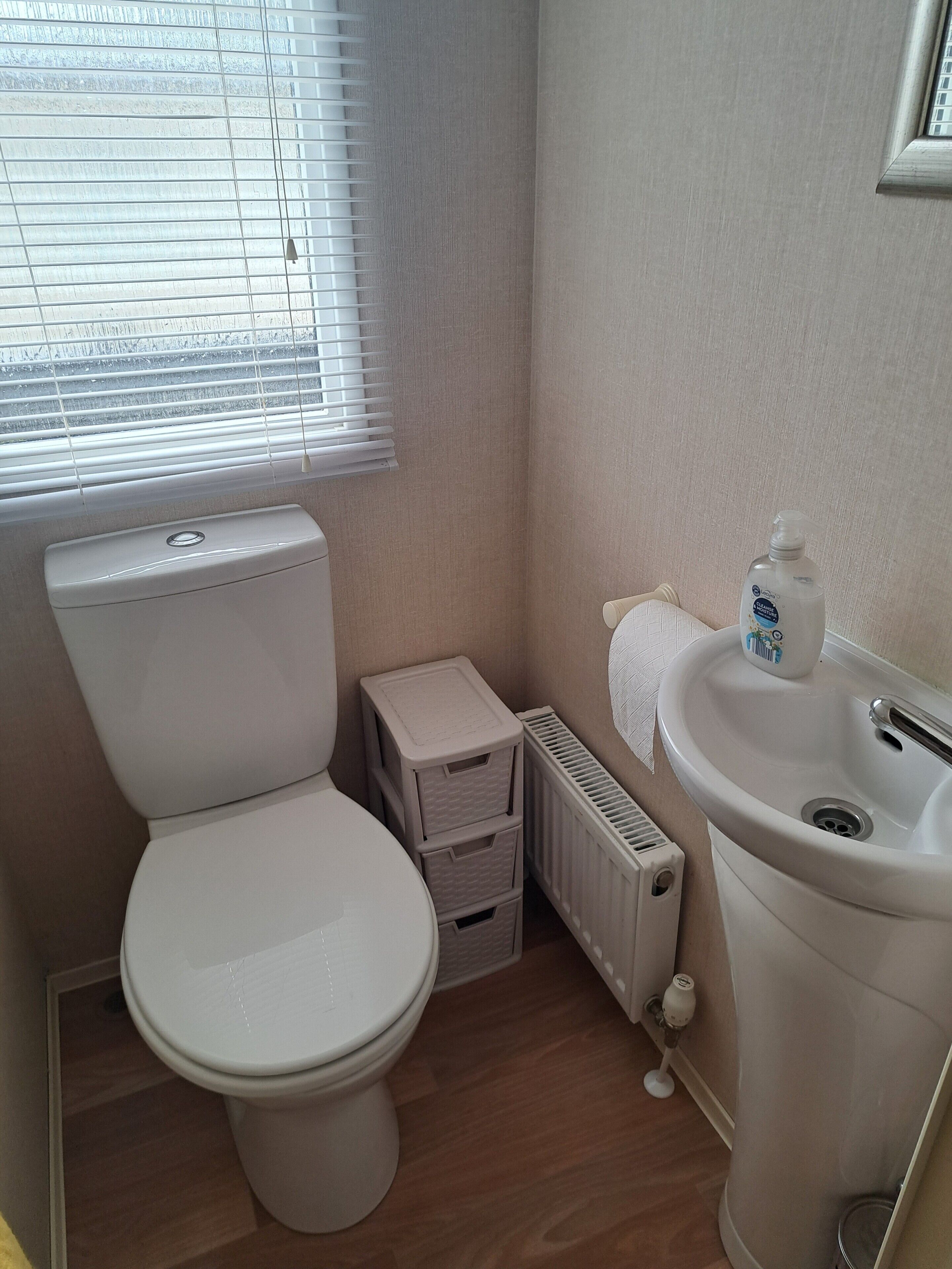 A small bathroom with a toilet, a radiator, a sink, and a window with blinds.