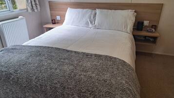 Un dormitorio con cama, mesita de noche y una ventana con cortinas.