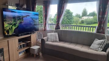 A living room with a flat-screen TV, a sofa, a small ottoman, and a window with curtains.