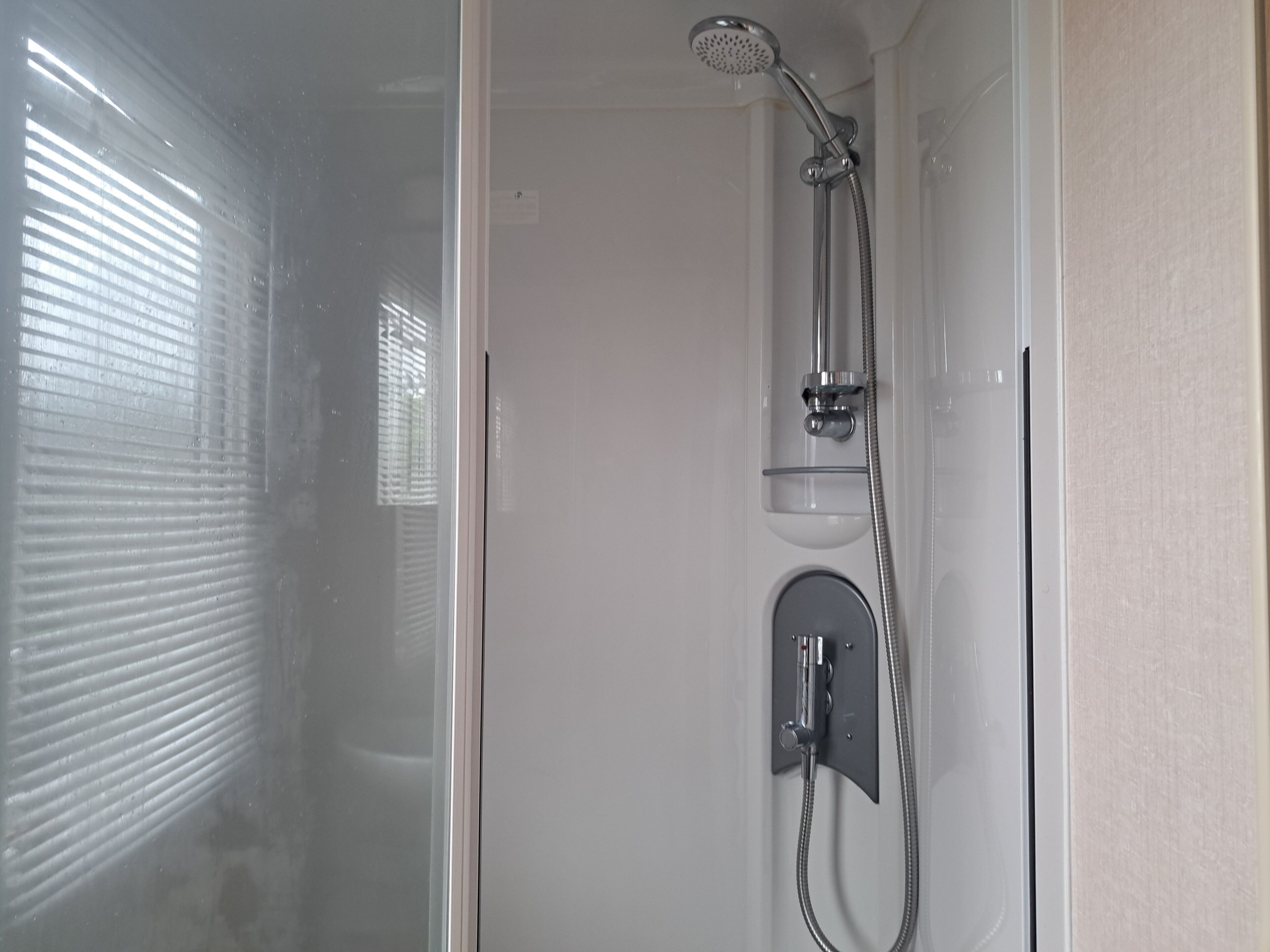 A shower enclosure with a handheld showerhead and a wall-mounted faucet.