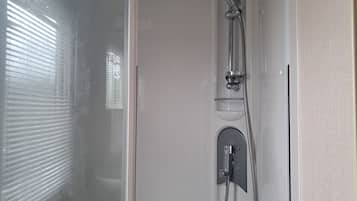 A shower enclosure with a handheld showerhead and a wall-mounted faucet.