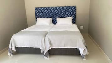 Una cama doble con cabecera estampada, dos almohadas y una colcha gris.