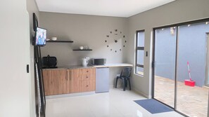 A compact kitchen with a microwave, toaster, and coffee maker on the counter, a small refrigerator, and a wall clock.