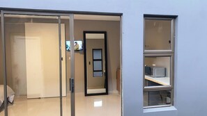 A room with a sliding door leading to a bathroom, a small window with a microwave, and a television mounted on the wall.