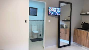 Un baño con inodoro, ducha, lavamanos y televisor montado en la pared.