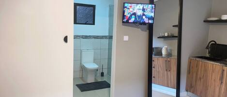 A bathroom with a toilet, a shower, a sink, and a television mounted on the wall.