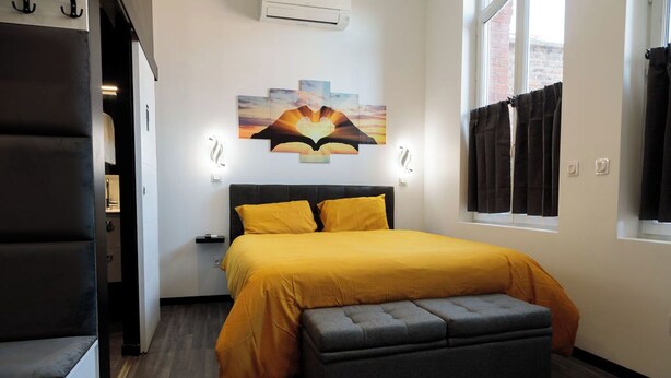 Ein Schlafzimmer mit einem Bett, einer Bank, einem Wandbild und einem Fenster mit Vorhängen.