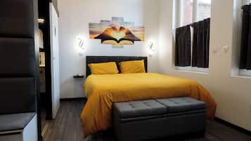 Une chambre à coucher comprenant un lit, un banc, une œuvre d’art accrochée au mur et une fenêtre avec des rideaux.
