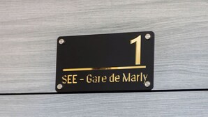 Ein schwarzes Schild mit goldener Schrift, das die Zimmernummer 1 und den Namen "SEE - Gare de Marly" angibt.