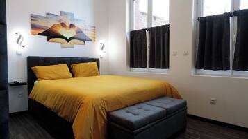 Un dormitori amb un llit, una panxa, una finestra amb cortines i una obra d'art penjada a la paret.