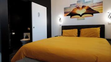 Une chambre d’hôtel avec un grand lit, une table de chevet, une lampe fixée au mur et un tableau au-dessus du lit.