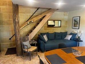 A room with a wooden staircase, a blue sofa, a dining table with placemats, and a chair with a patterned cushion. - Holiday Home 'Maison Bord’Eau -  Bord De Dordogne' with Shared Garden, Wi-Fi and Air Conditioning (Saint-André-de-Cubzac)