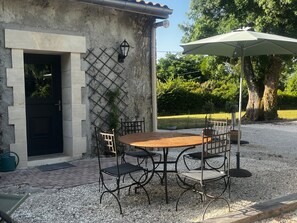 Une terrasse avec une table et des chaises, une porte et un luminaire fixé au mur.