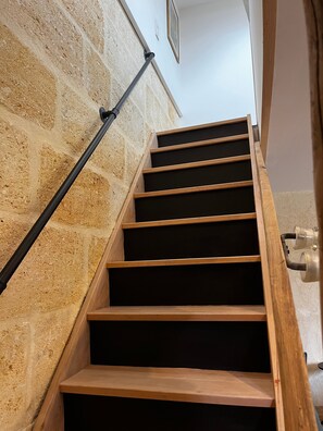 A wooden staircase with a black handrail against a textured stone wall. - Holiday Home 'Maison Bord’Eau -  Bord De Dordogne' with Shared Garden, Wi-Fi and Air Conditioning (Saint-André-de-Cubzac)